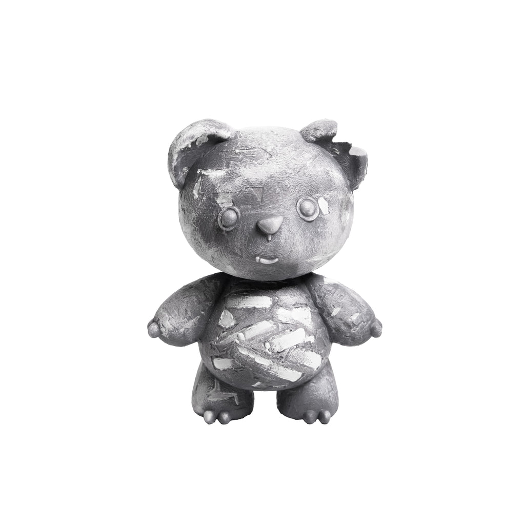 A distressed, weathered gray teddy bear figurine with chipped paint and a bandage pattern on its belly, isolated on a white background.