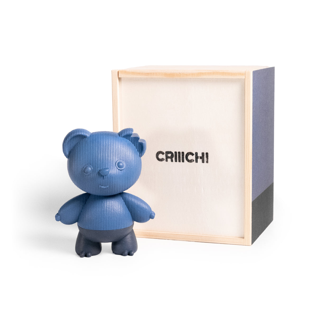 A blue bear-shaped collectible figure with a textured surface stands in front of its light wood and gray box packaging, which features the brand name 'CRIIICHI' printed on the front.