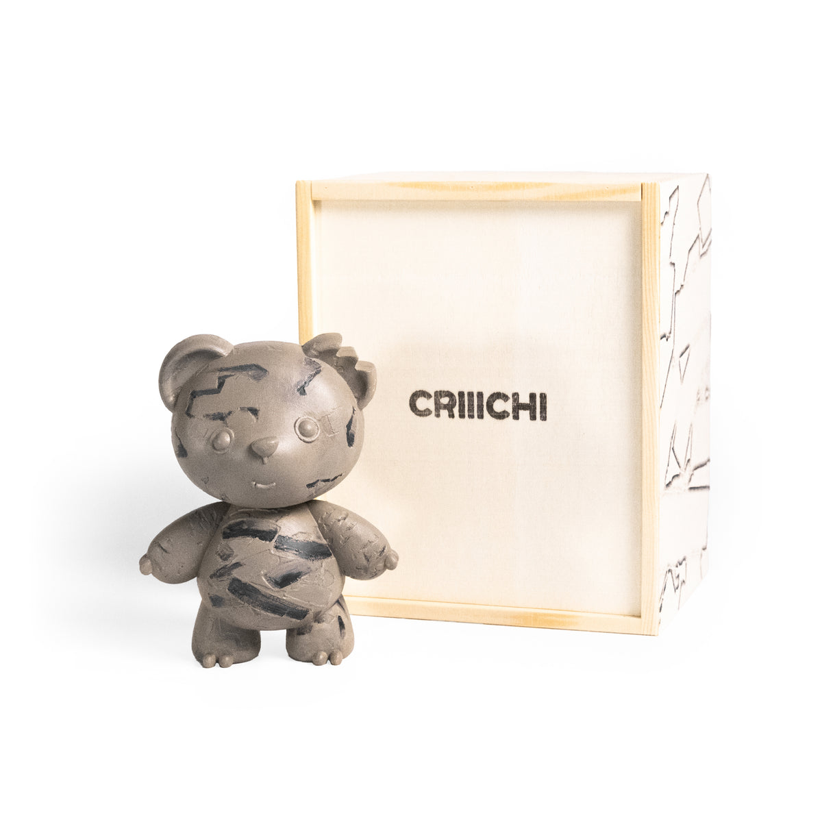 A small gray teddy bear figurine with black scratch-like markings stands in front of a light wood box with the brand name 'CRIIICHI' printed on the inside.