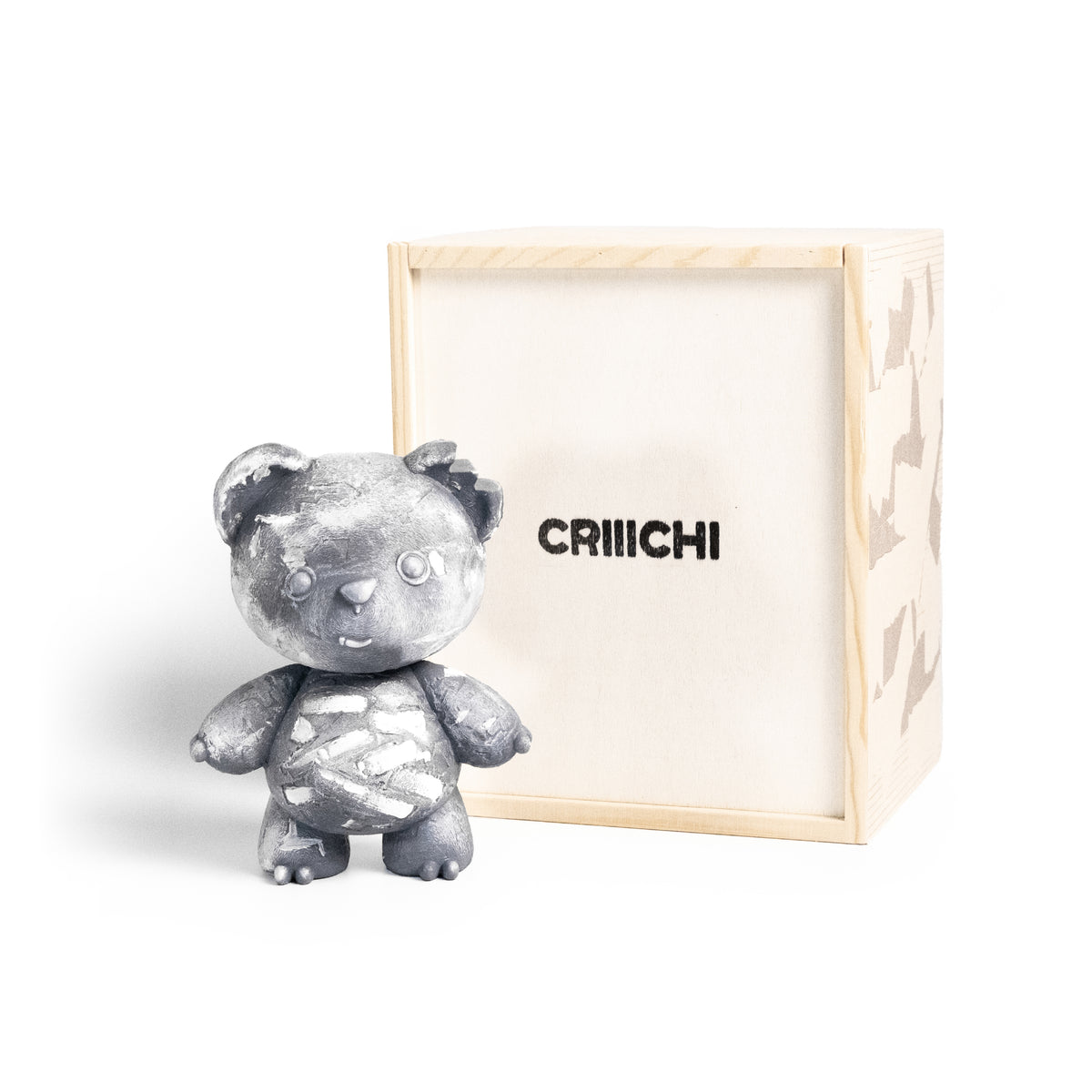 A greyish spray bear figurine with a textured, painted finish stands in front of its light wood and cream-colored presentation box, which features the brand name 'CRIIICHI' printed in black.