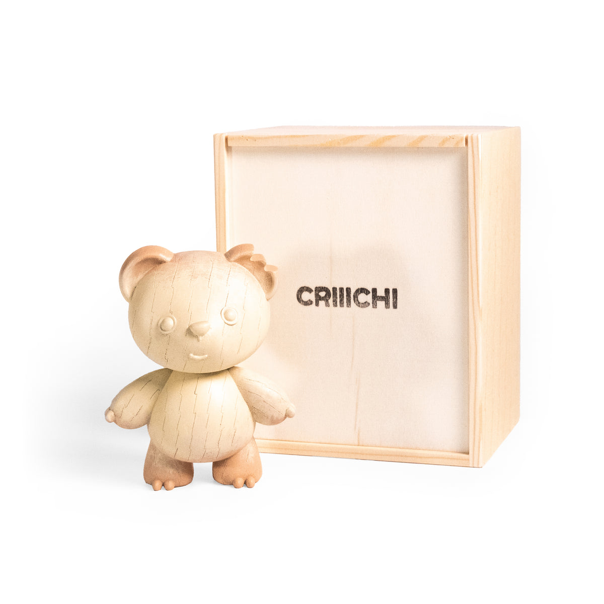 A small carved wooden teddy bear figurine standing in front of its light natural wood presentation box, which has the brand name 'CRIIICHI' printed on the front, set against a clean white background.