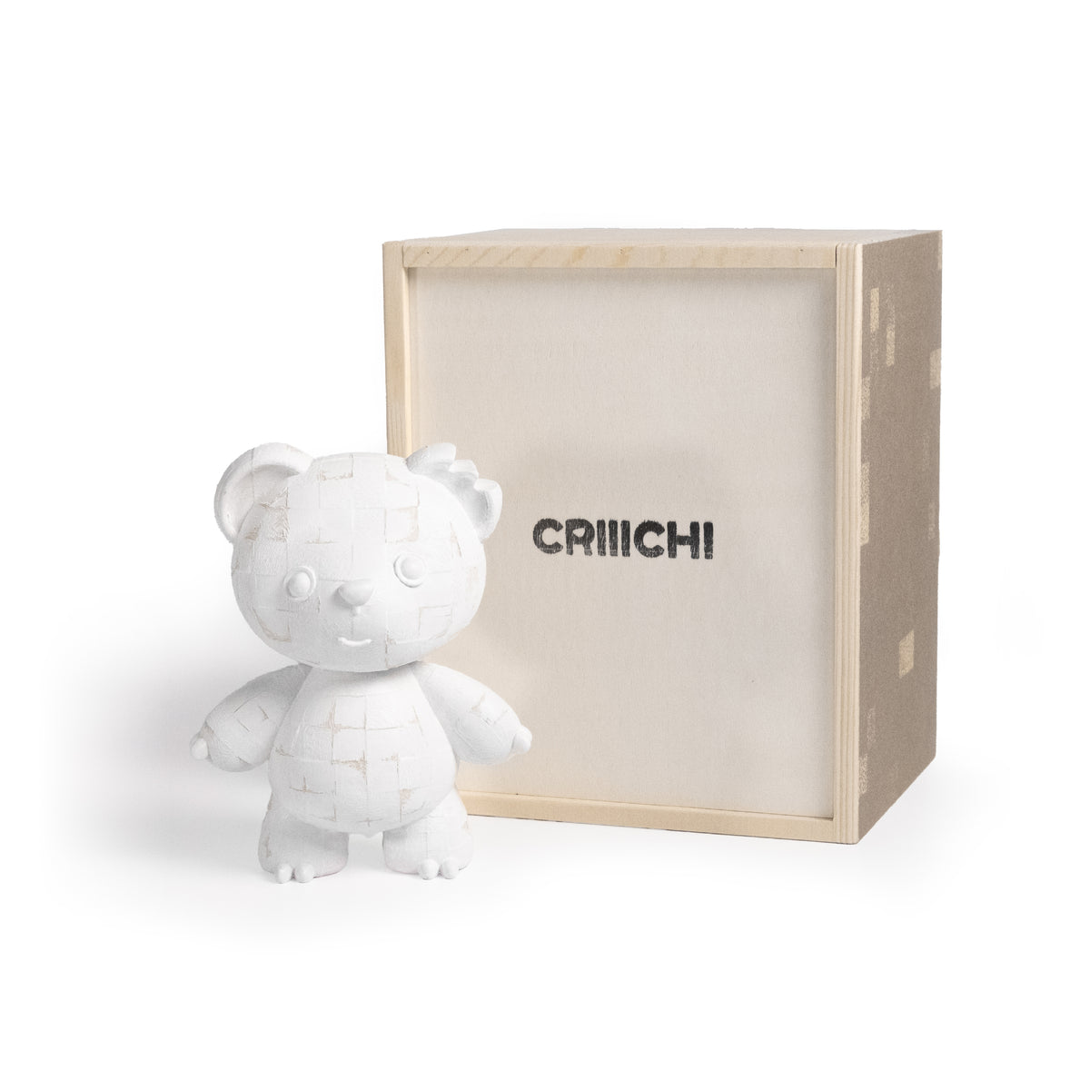 A white ceramic bear figurine with a grid-like pattern on its body, standing next to its light wood and beige fabric box which features the brand name 'CRIIICHI' in black.