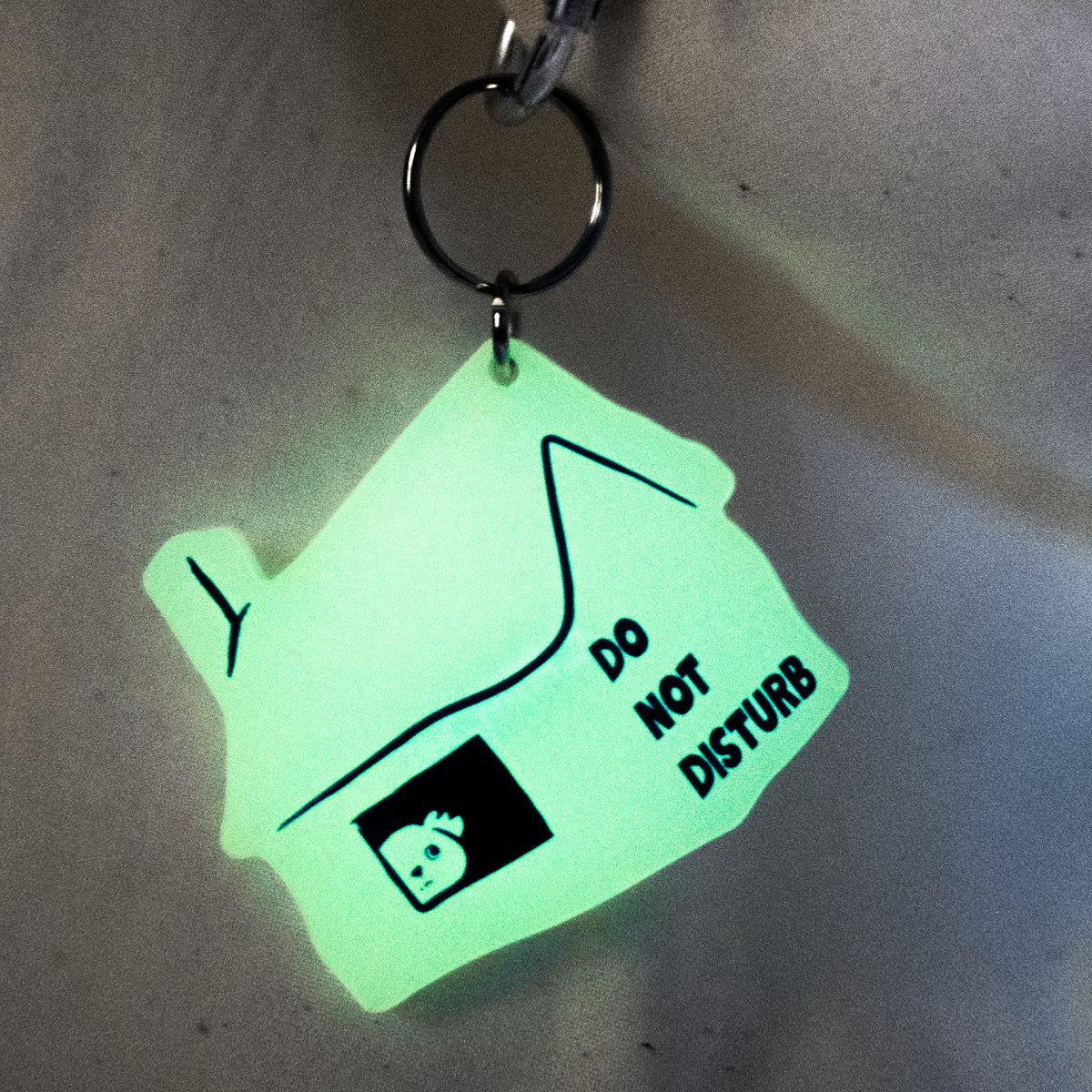 A house-shaped keychain with a glowing green finish, featuring a skull icon and the text 'DO NOT DISTURB' on a dark background.